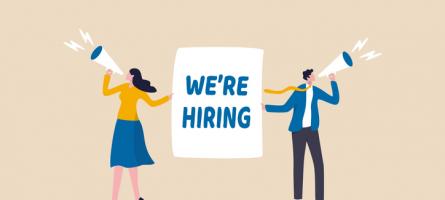"We're Hiring" Sign being held by two people with megaphones